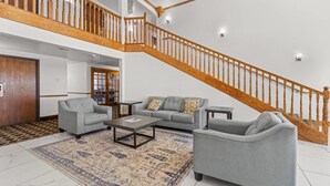 A spacious living area with a high wooden staircase, a grey sofa set, and a patterned rug. - Quality Inn Dodge City (Dodge City)
