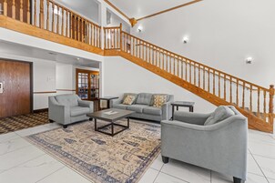 Un amplio espacio de sala con una escalera de madera alta, un conjunto de sofás grises y un tapete estampado.