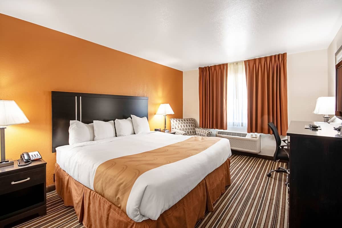 A hotel room with a large bed, two bedside tables with lamps, a desk, and a chair.