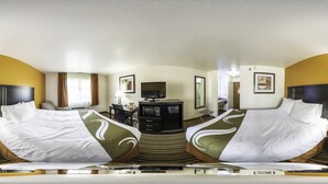 A hotel room with a large bed, a desk with a computer, a television, and a bathroom visible through an open door. - Quality Inn Dodge City (Dodge City)