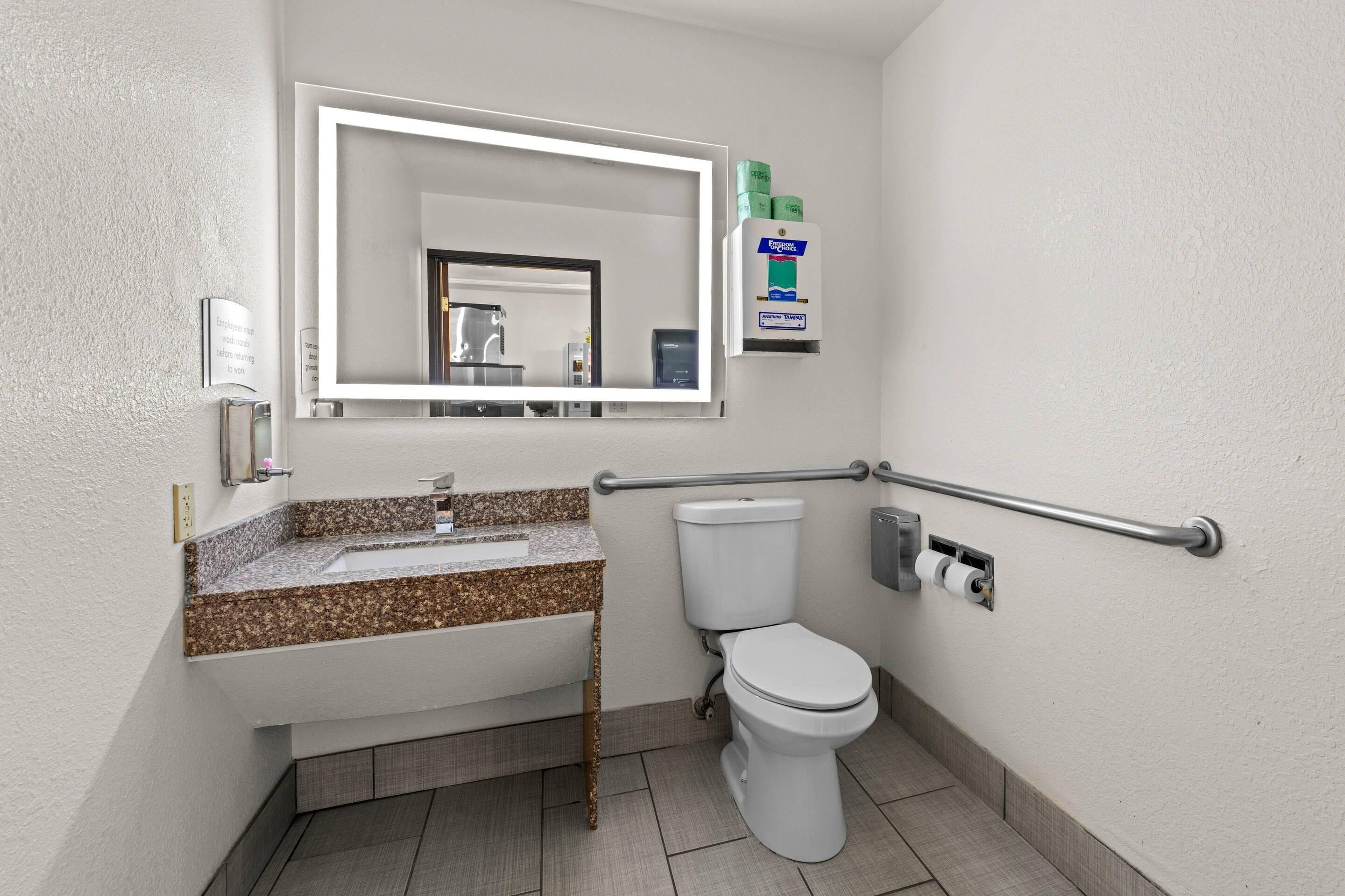 Un baño con lavamanos, espejo, inodoro y dispensador de gel antibacterial.