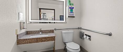 Un baño con lavamanos, espejo, inodoro y dispensador de gel antibacterial.