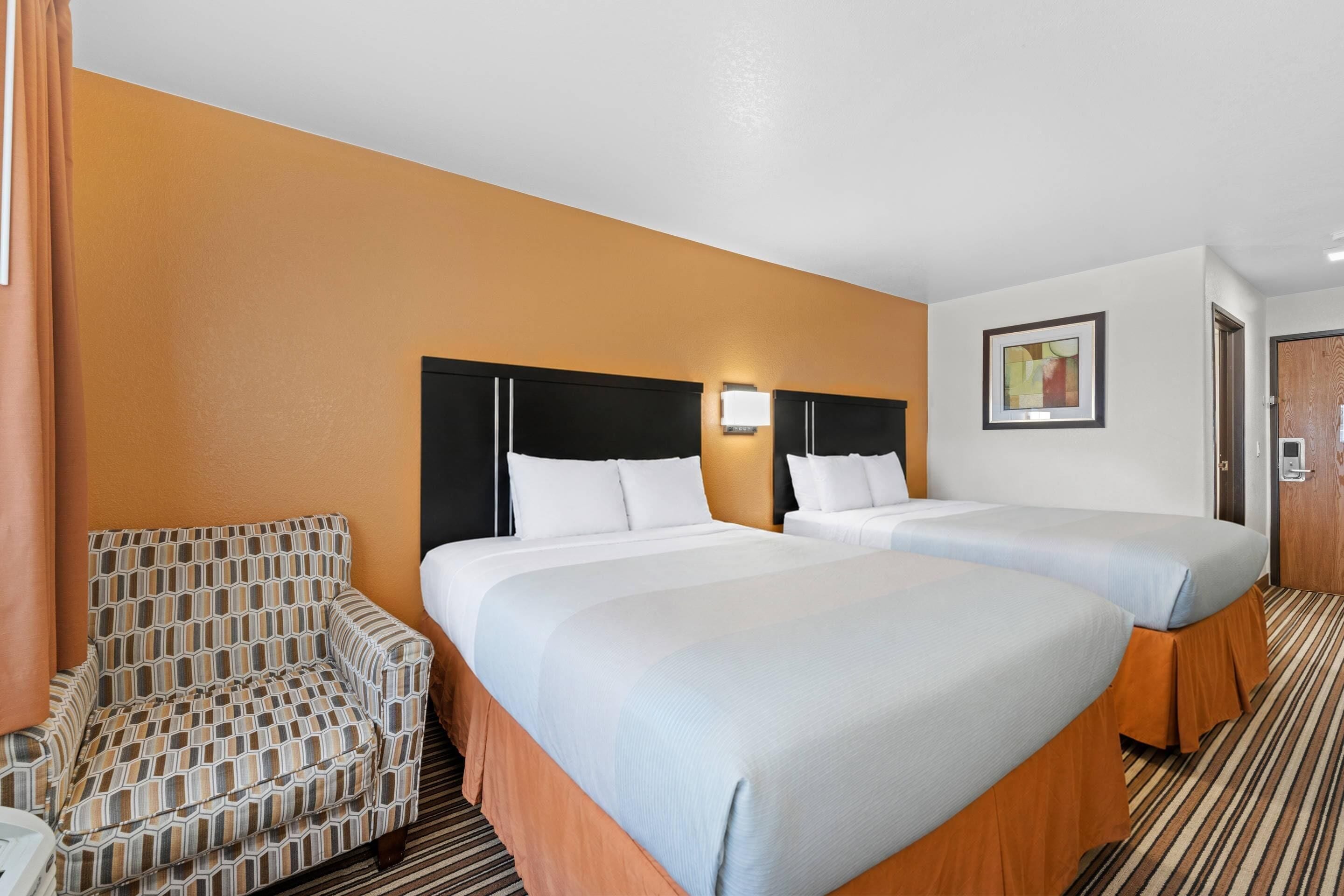 A hotel room with two beds, a chair, and a framed picture on the wall.