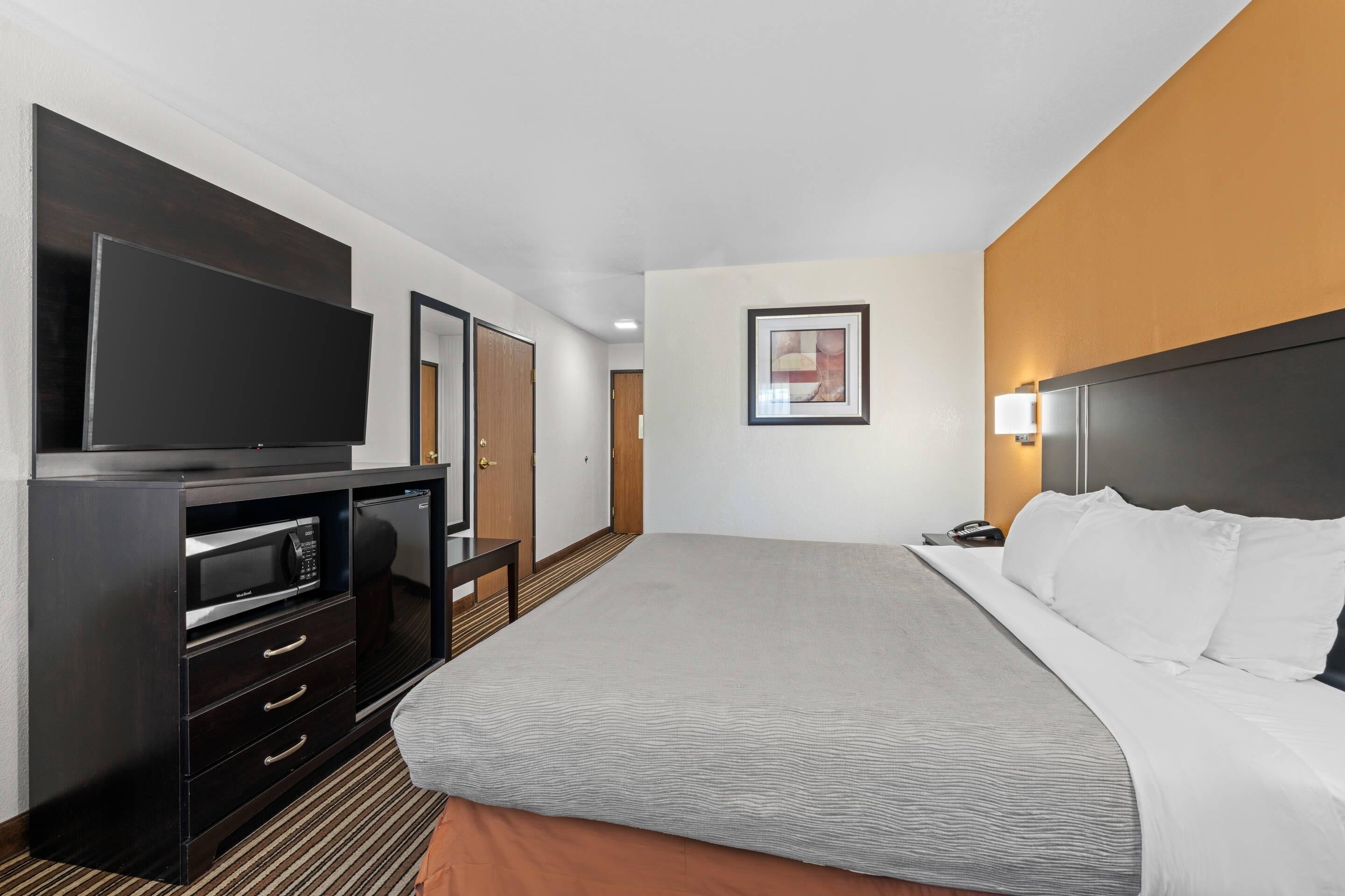 Ett hotellrum med en säng, en TV, en minibar och en dörr.