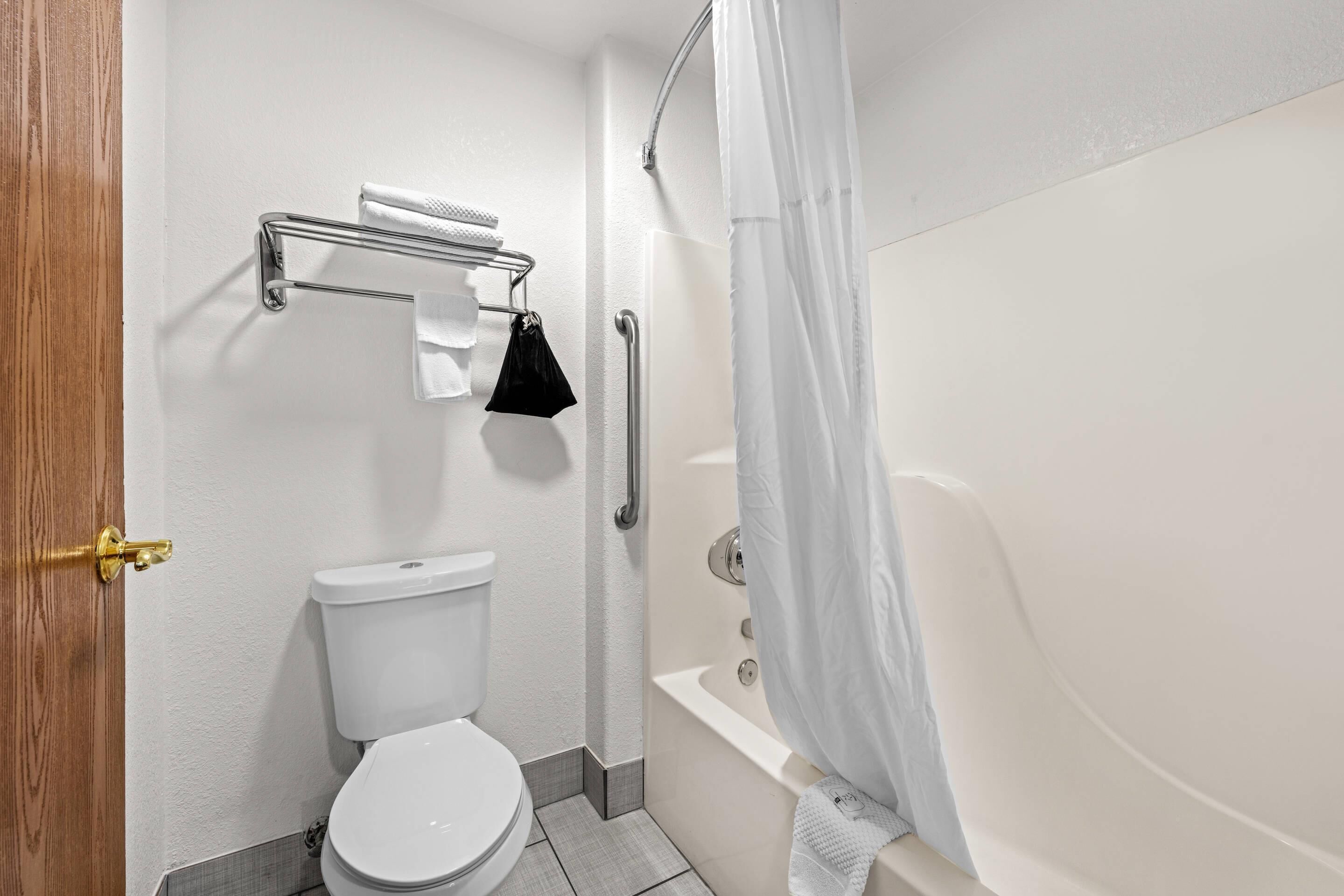 A bathroom with a toilet, a bathtub, a shower curtain, and a towel rack.