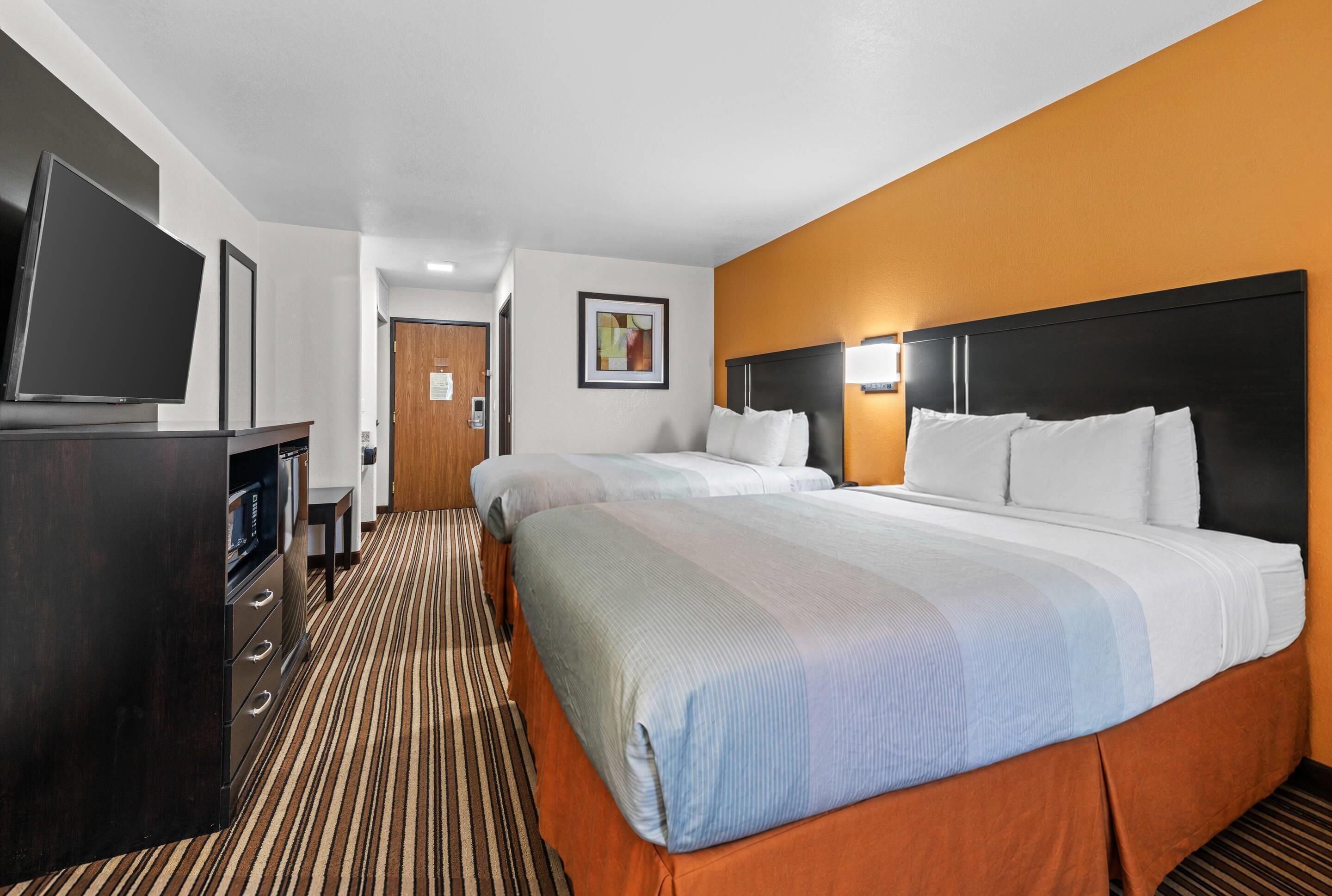 A hotel room with two beds, a TV, a desk, and a door.