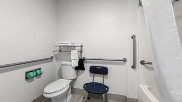 A bathroom with a toilet, a shower, a grab bar, a wheelchair-accessible chair, and a towel rack.