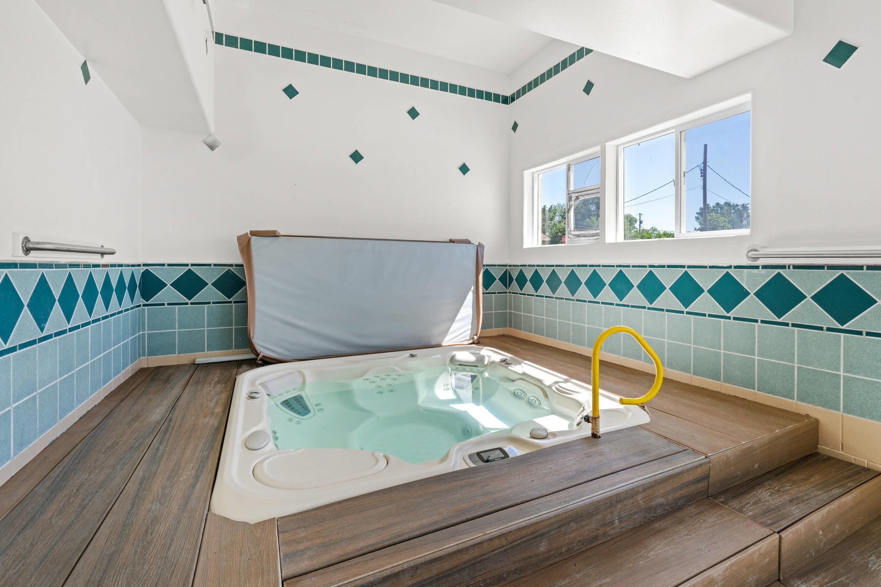 A hot tub with steps, a window, and a tiled wall.