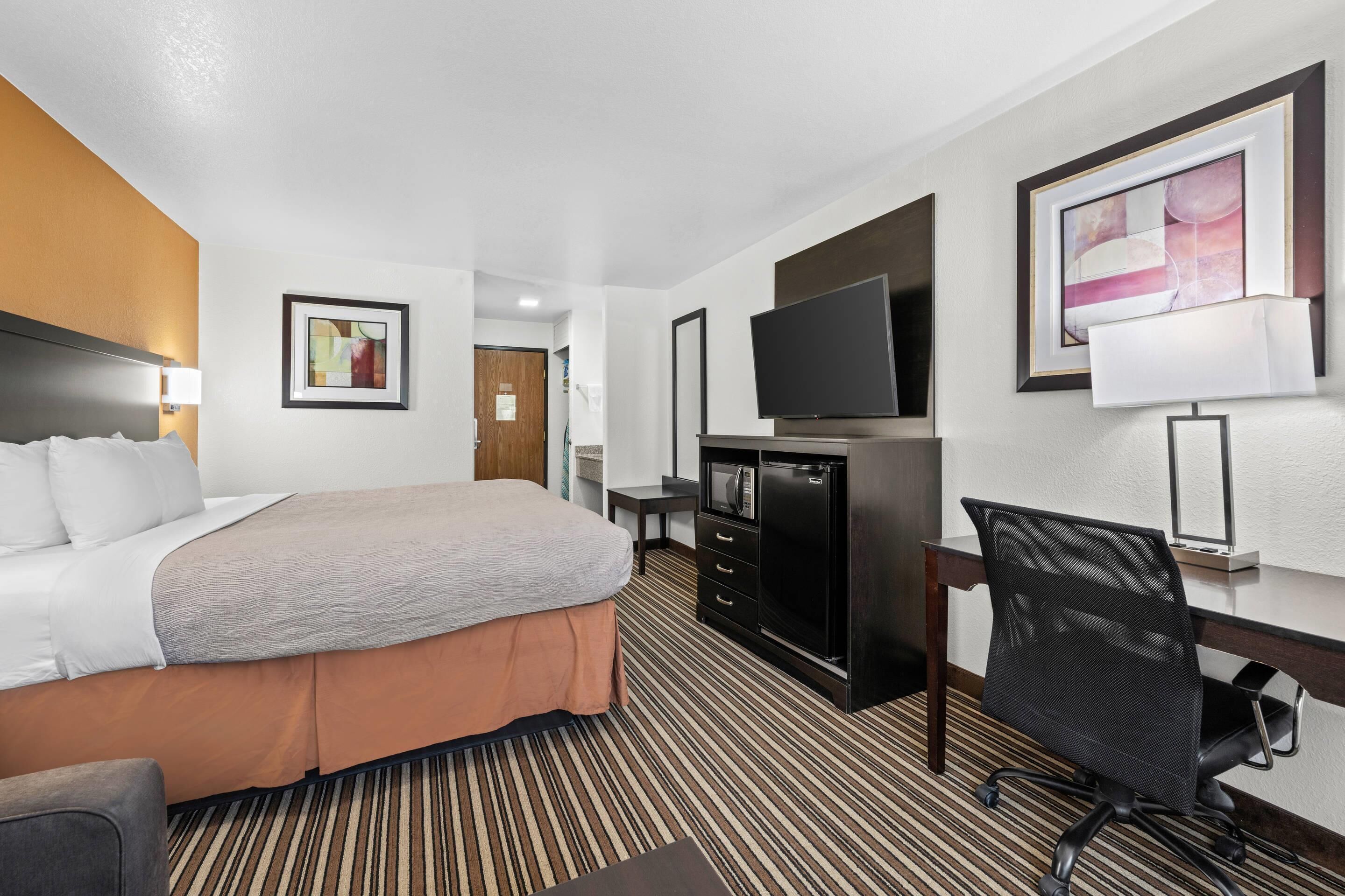 Een hotelkamer met een bed, bureau, stoel, televisie en kunstwerken aan de muren.