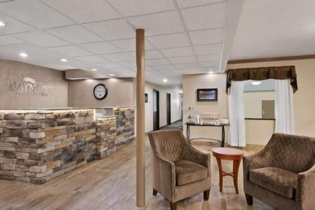 Un espace d’accueil avec un mur en pierre, une horloge et deux fauteuils disposés autour d’une petite table.