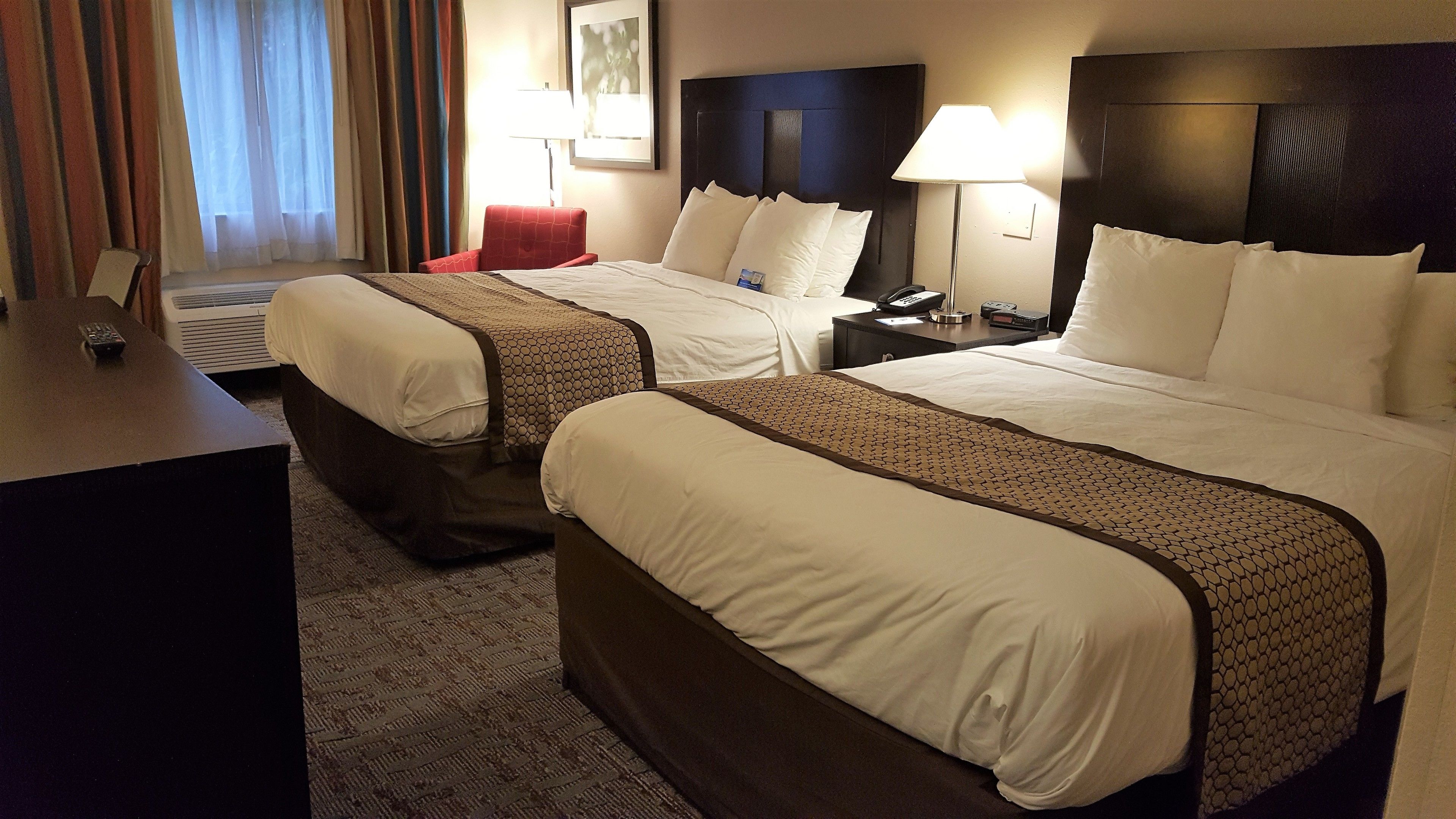 Quarto de hotel com duas camas, uma escrivaninha, uma luminária e um telefone.