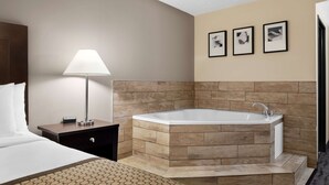 Habitación de hotel con una cama grande, una mesita de noche con lámpara, una bañera en esquina y tres cuadros enmarcados en la pared.