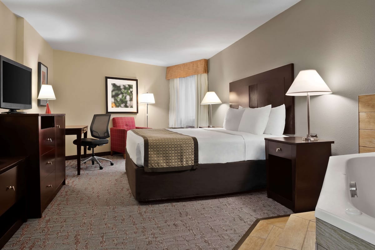 Une chambre d’hôtel comprenant un lit, des lampes de chevet, un bureau avec une chaise, une télévision et une salle de bain avec une baignoire.
