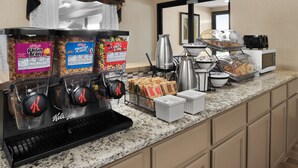 Una barra de desayuno con dispensadores de cereales, una cafetera, un tostador y una exhibición de pan.