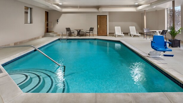Una piscina interior con agua cristalina y azul, rodeada de sillones de descanso y una pequeña mesa.