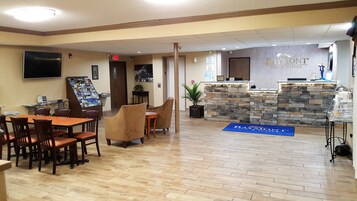 Un vestíbulo de hotel con una recepción, un área de descanso con mesas y sillas, y un televisor en la pared.