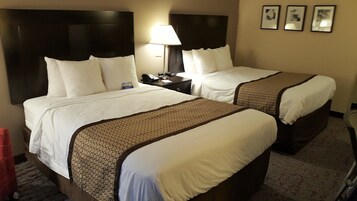 Una habitación de hotel con dos camas, cada una con ropa de cama blanca y colchas marrones estampadas. Hay una mesita de noche con una lámpara y un teléfono.