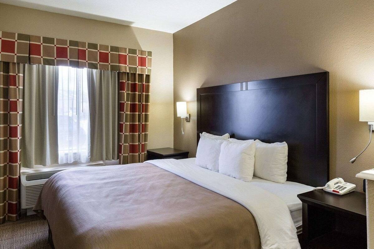 A hotel room with a large bed, a nightstand with a phone, and a window with curtains.