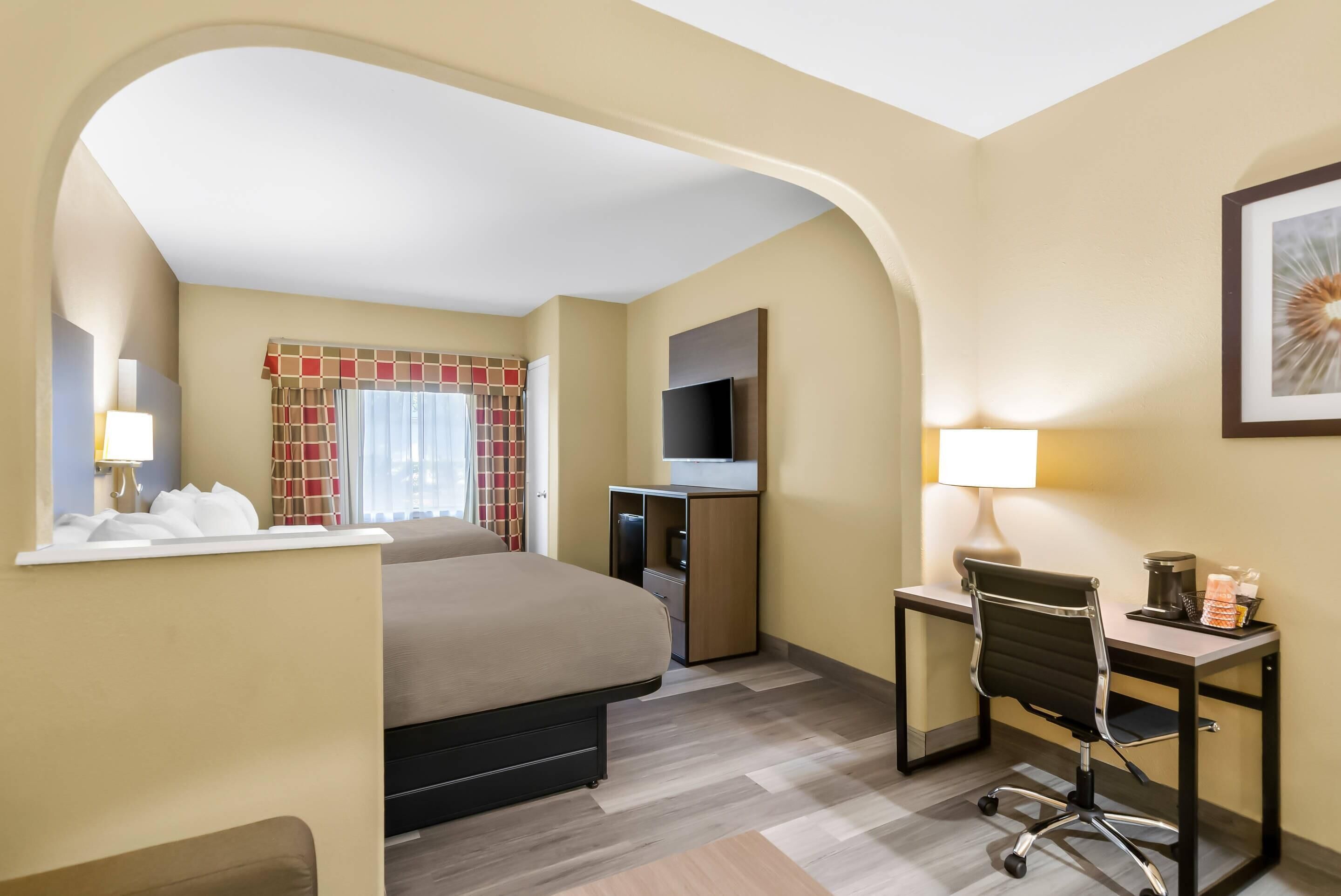 A hotel room with a bed, desk, chair, TV, and a window with curtains.