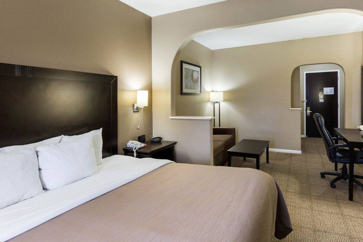A hotel room with a large bed, a desk, a chair, and a small table.