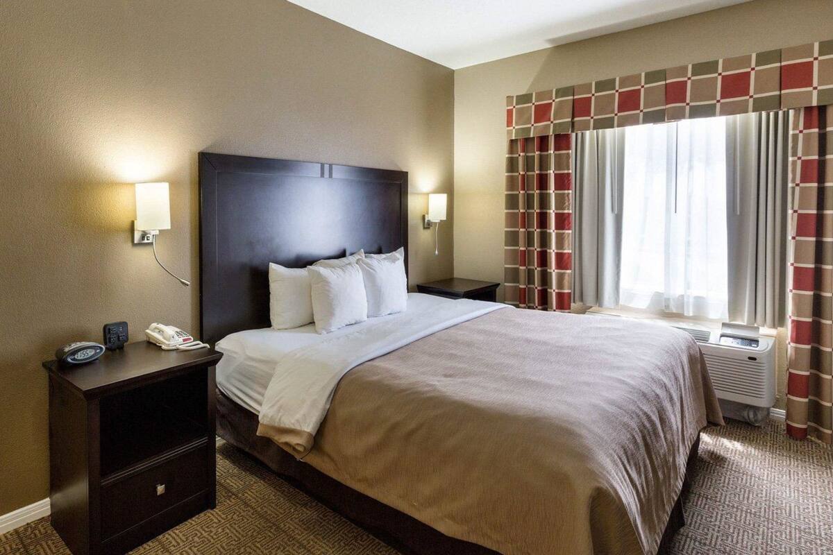 A hotel room with a large bed, bedside tables, a telephone, and a window with curtains.