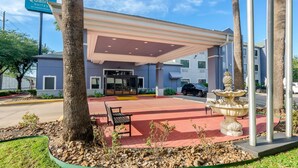 A hotel entrance with a covered waiting area, a bench, and a decorative fountain. - Quality Suites Houston NW Cy-Fair (Houston)