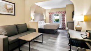 A modern hotel room with a sofa, a bed, a desk, and a small table. There is a picture on the wall and a window with curtains. - Quality Suites Houston NW Cy-Fair (Houston)