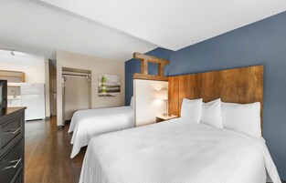 Habitación de hotel con dos camas, cabecero de madera, escritorio y refrigerador.