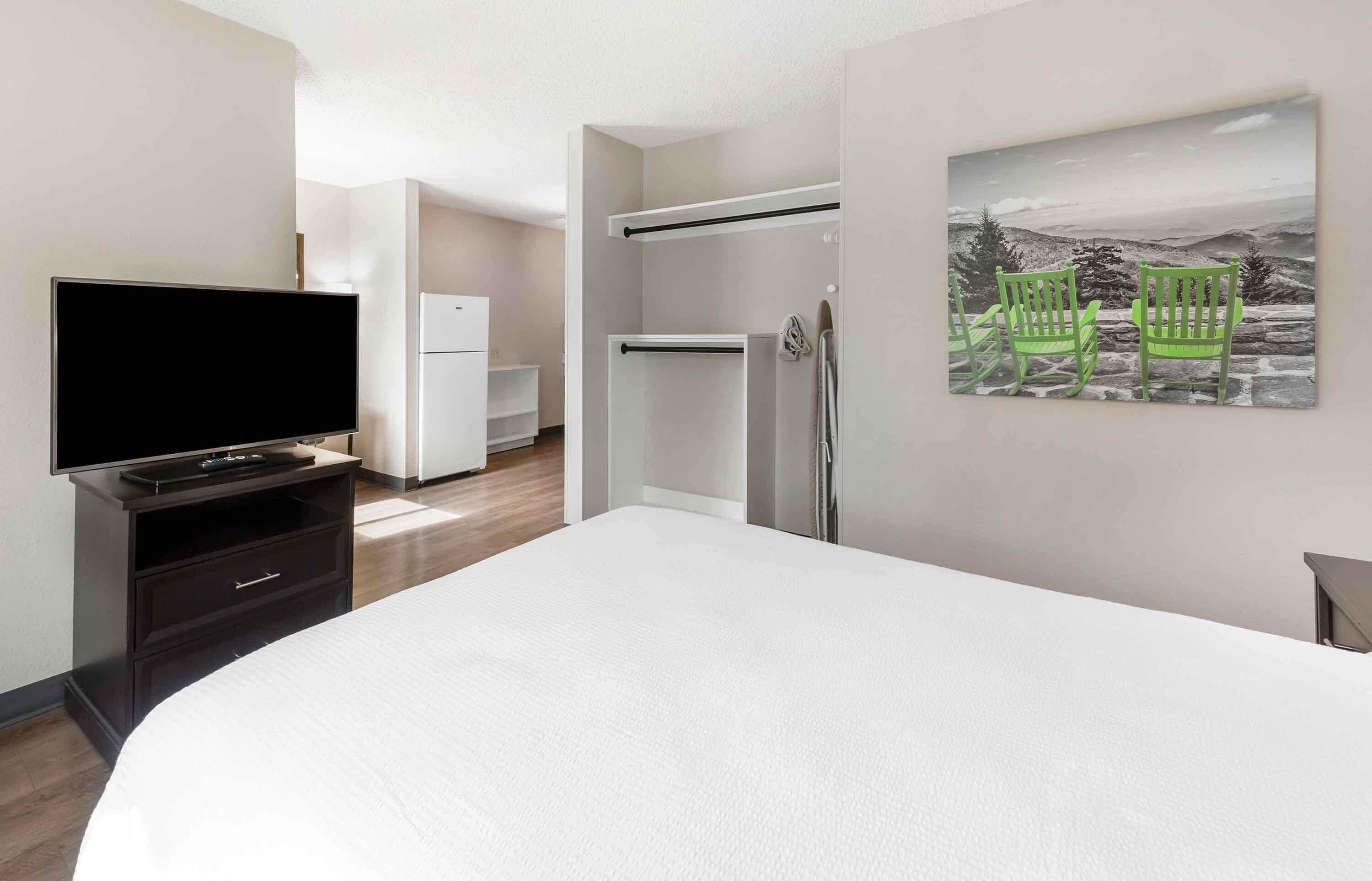 Ein Hotelzimmer mit einem Bett, einem Fernseher, einem Kleiderschrank, einer Dusche und einem Bild von Stühlen.