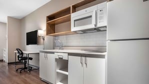 A modern kitchen with white cabinets, a microwave, a sink, and a chair. - Extended Stay America Premier Suites - Miami - Airport - Miami Springs (Miami Springs)