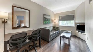 A hotel room with a desk, office chair, sofa, and a TV mounted on the wall. - Extended Stay America Premier Suites - Miami - Airport - Miami Springs (Miami Springs)