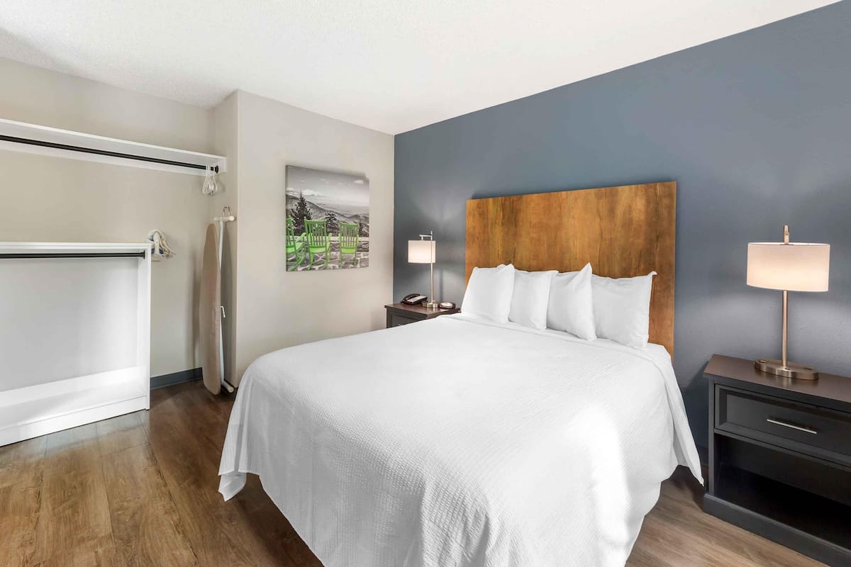 A hotel room with a large bed, two bedside tables with lamps, a wooden headboard, a painting on the wall, and a sliding door.