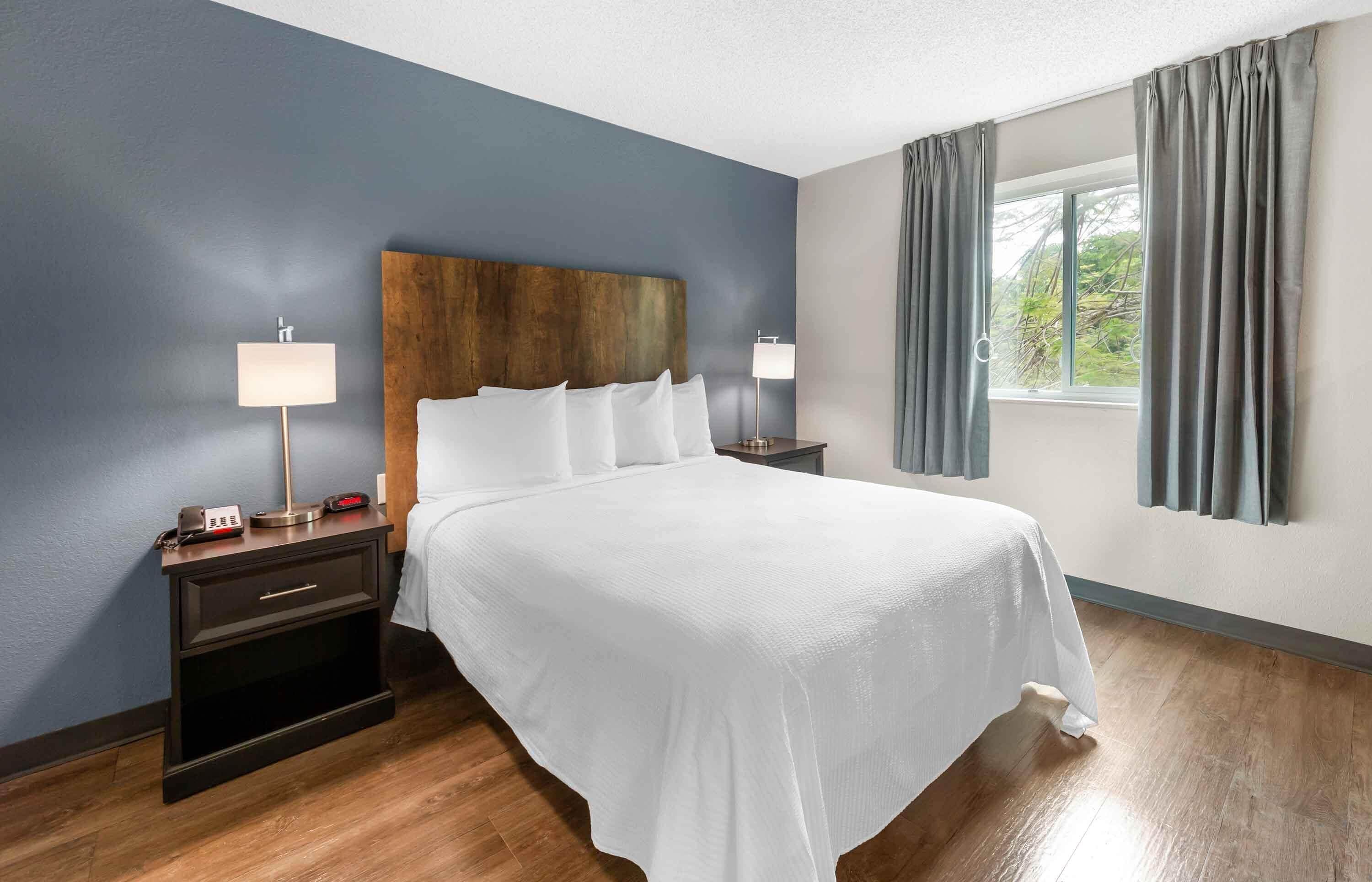 A hotel room with a large bed, two bedside tables with lamps, a wooden headboard, and a window with curtains.