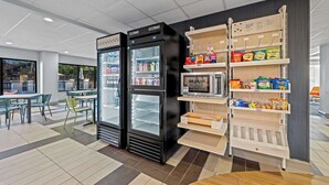 A modern food service area with two black refrigerators, a microwave, and shelves stocked with snacks and beverages. - Spark by Hilton Tuscaloosa University (Tuscaloosa)