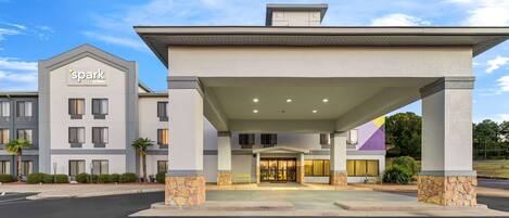 A hotel entrance with a covered area and a 'Spark' sign, featuring a modern architectural design with stone accents and a clear sky.