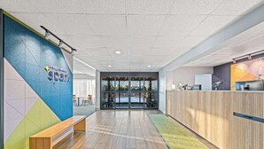 A modern reception area with a wooden bench, a colorful wall, and a glass door leading to an outdoor space. - Spark by Hilton Tuscaloosa University (Tuscaloosa)