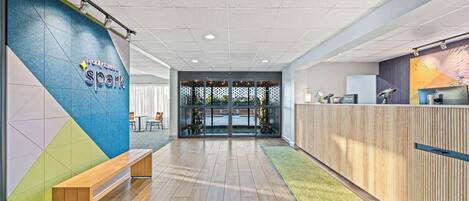 A modern reception area with a wooden bench, a colorful wall, and a glass door leading to an outdoor space.