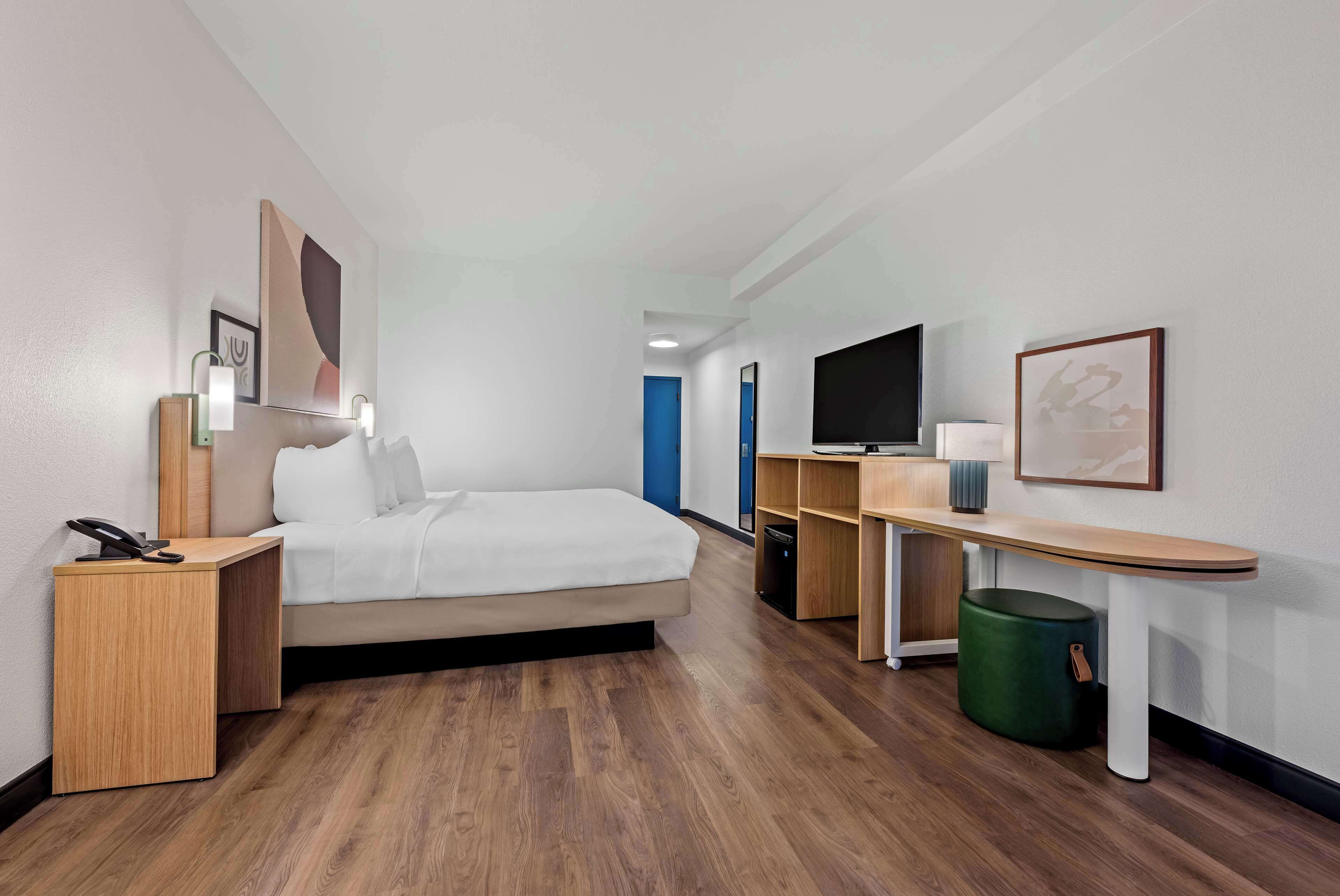 Una habitación de hotel con cama, mesita de noche, lámpara, televisor y un escritorio pequeño con una silla.