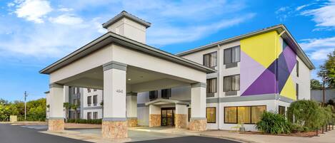 A modern hotel with a covered entrance, a stone facade, and a colorful geometric design on one side.