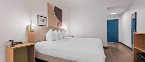 Ein Hotelzimmer mit einem großen Bett, einem Nachttisch mit Telefon, einer Wandleuchte und einer blauen Tür im Hintergrund.