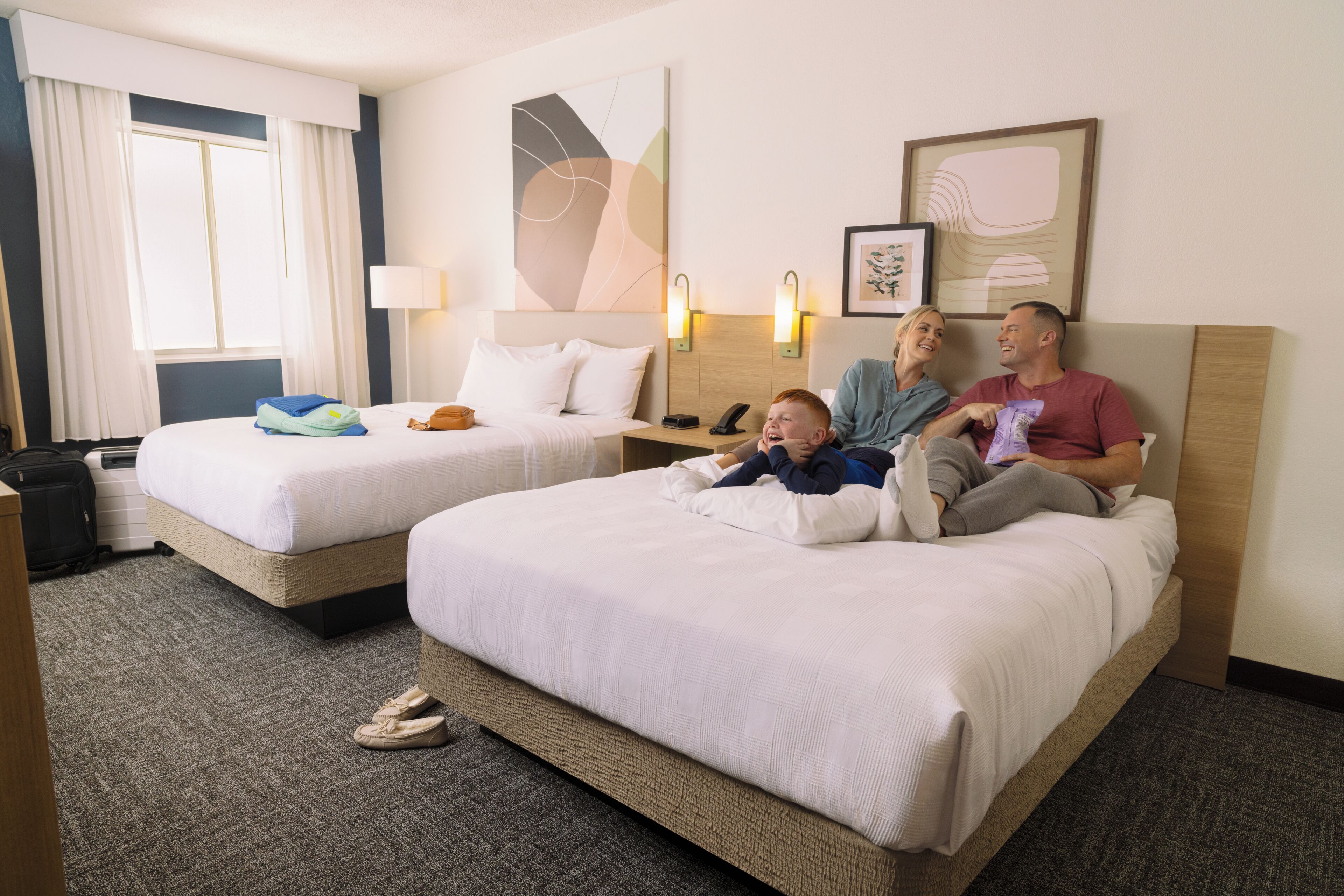 Hotellihuone, jossa on kaksi sänkyä, työpöytä ja ikkuna, jossa on verhot.