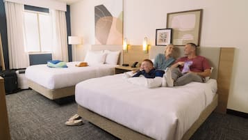 A hotel room with two beds, a desk, and a window with curtains.