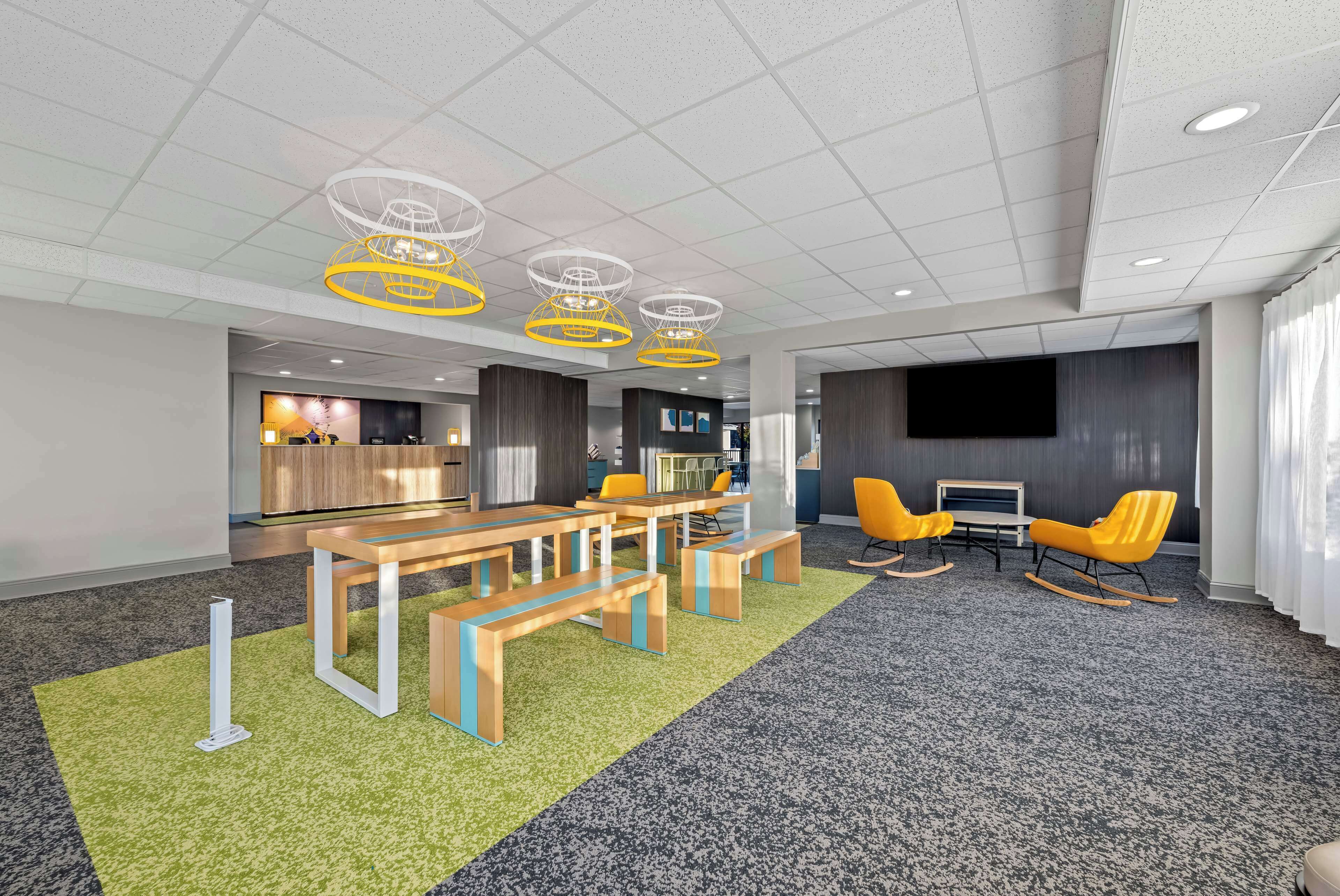 A modern conference room with a large screen, yellow chairs, and a wooden table with benches.