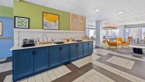A modern kitchen area with a blue cabinet, a countertop with coffee makers, and a sign that says "Delight in the day". - Spark by Hilton Tuscaloosa University (Tuscaloosa)