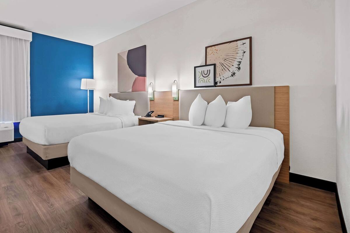 Habitación de hotel con dos camas, una pared de acento azul y obras de arte en la pared.