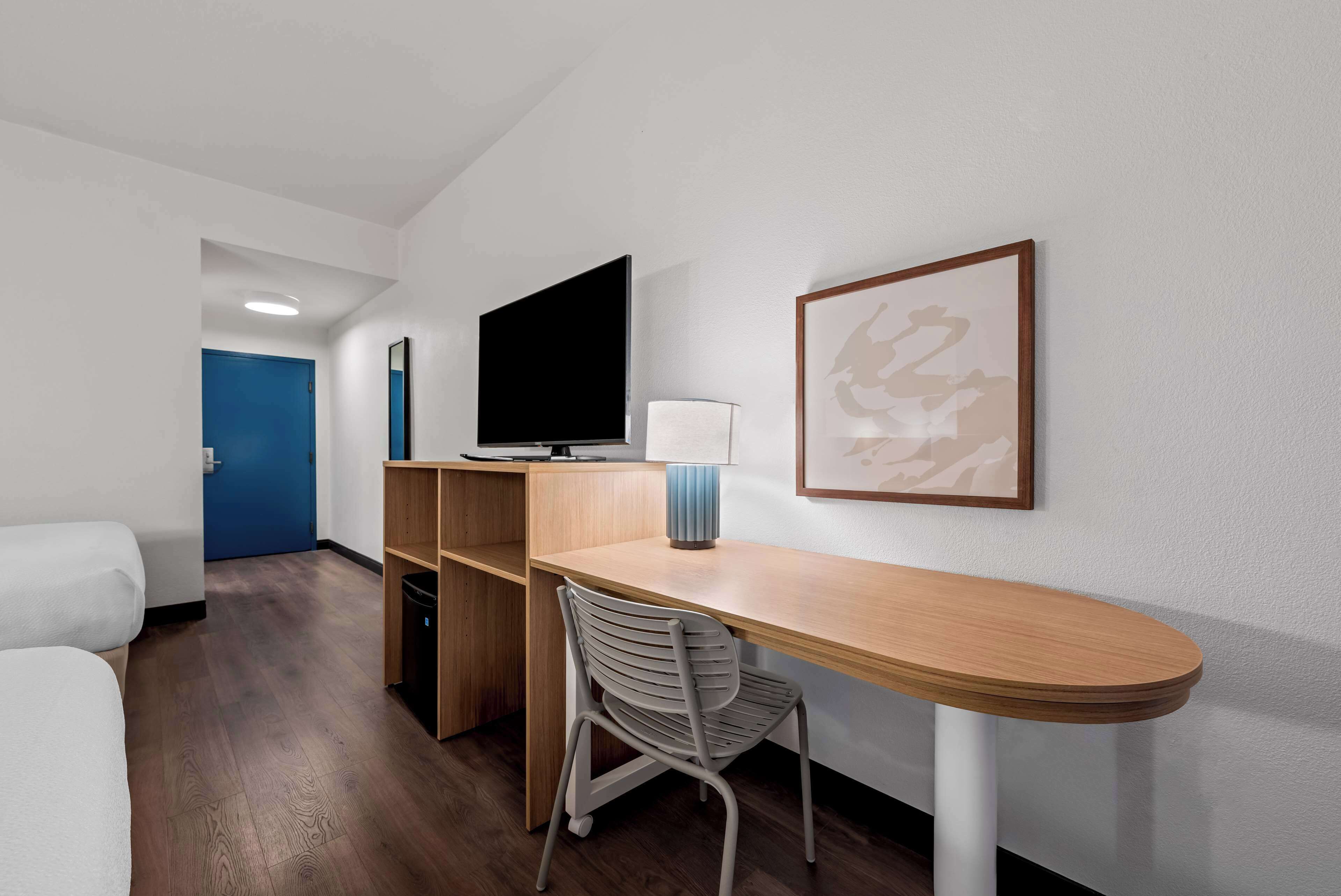 Una camera d'albergo con una scrivania in legno, una televisione, una sedia, un letto e una porta blu.