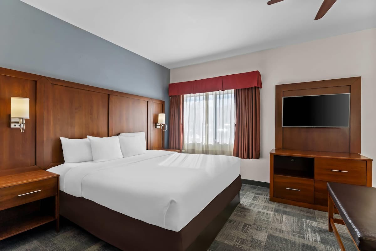 A hotel room with a large bed, wooden headboard, bedside tables, a TV, and a desk.
