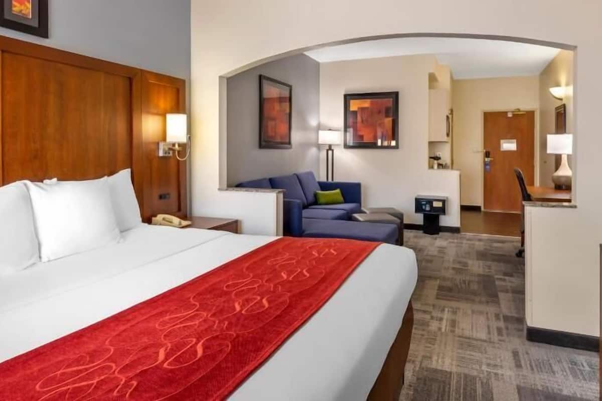 A hotel room with a large bed, a desk, a chair, and a sofa.