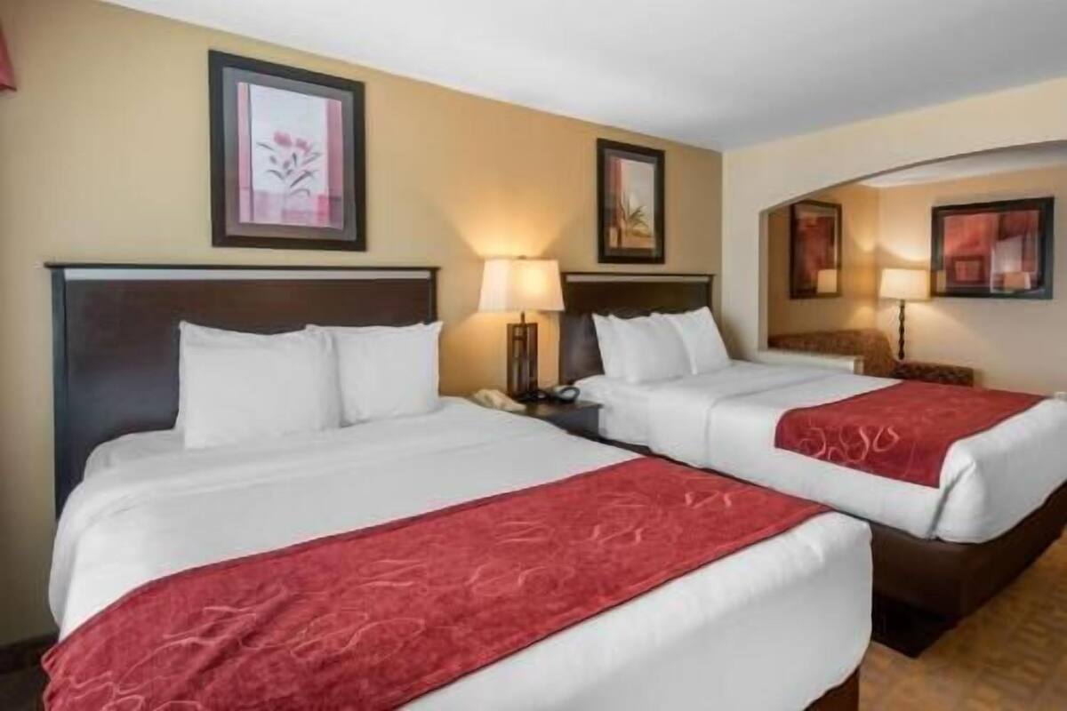 A hotel room with two beds, a nightstand with a lamp, and framed artwork on the walls.