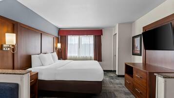 A hotel room with a large bed, wooden headboard, bedside lamps, a flat-screen TV, and a desk with a chair.